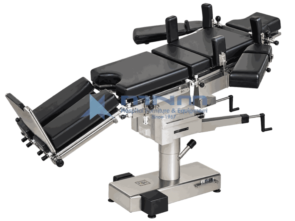Operating table with black upholstered multi section top, shoulder supports, arm boards and leg troughs fitted, on a low rectangular stainless base with foot pedals