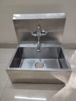 Stainless steel single bowl scrub sink photographed installed on a hospital floor, showing the finished unit in use