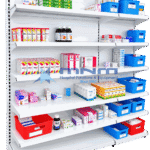 Single sided gondola rack with white slatted back panel and six shelves stocked with medicine cartons, syrup bottles and labelled dispensing baskets